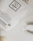 Só Clean powdered laundry soda packaging on a light background with felt dryer balls and some white powdered product.