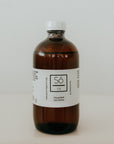 An amber glass bottle of Só Oil Unscented Face & Body Oil with a white label and white cap, set against a plain light gray background.