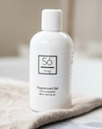 A white bottle of Só Magnesium Gel with on beige fabric with a blurred background.