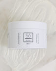 A white plastic jar of Só Butter Bergamot Vanilla body butter, placed on top of a textured background of white whipped product