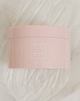 A pink plastic jar of Só Butter Island Coconut body butter, placed on top of a textured background of white whipped product