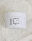 A white plastic jar of Só Butter Unscented body butter, placed on top of a textured background of white whipped product