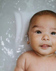 A close-up of a baby laying in a white bathtub with water around them.