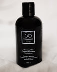 A black bottle of Só Soap foaming hand wash concentrate in Rosemary Mint scent, standing upright styled on a blurry white background.