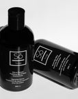 Two black bottles of Só Soap hand wash concentrates, one standing upright and the other lying on its side, on a white background.