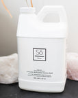 A white plastic bottle labeled 'Só Clean' with 'Lavender All Purpose Cleaner' written on it, placed between a white rock and a pink rock on a dark gray surface.