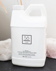 A white bottle labeled 'Só Clean Lavender All Purpose Cleaner', placed on a dark surface with a white and a pink rock in the background