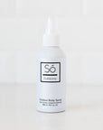 A white bottle of Só Outdoors Outdoor Body Spray with a white nozzle cap, standing on a white surface against a white tiled background.