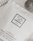 Só Clean oxygen whitening powder packaging with felt dryer balls on a neutral surface.