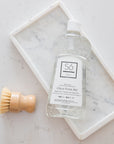 Bottle of branded Só Clean itrus Rinse Aid with a wooden brush on a marble surface