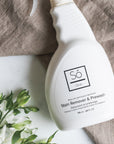 White spray bottle branded with 'Só Clean Stain Remover + Prewash' on a light marble background with light brown fabric and floral greenery.