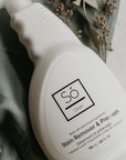White spray bottle branded with 'Só Clean Stain Remover + Prewash' on a light marble background with green fabric and greenery.