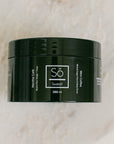 A 250 ml black jar of Só Sweet Mint Coffee body scrub, resting on a light beige marble surface.