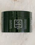 A 250 ml black jar of Só Sweet Rosemary Eucalyptus body scrub, resting on a light beige marble surface.