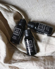 Three small black bottles of Só Luxury essential oils placed on a beige cloth surface.