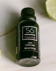 A black bottle of Só Essential Oil labelled Lime 30 ml on a light gray background with a half cut lime in the top corner.