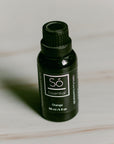 A black bottle of Só Essential Oil labelled Orange 30 ml on a light grey background