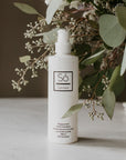 A white bottle of branded 'Só Sanitizer' with a pump top styled on a marble surface with natural greenry