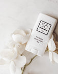 A white plastic deodorant style container branded Só Salve Fire Salve a warming muscle salve in 10 g twist-up stick styled on a marble background with white flowers.
