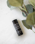 A black lip balm stick with a white logo and text, labeled 'Só Lippy Lavender Lip Balm', placed on a light marble surface next to green eucalyptus leaves.