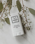 A white plastic deodorant style container branded Só Salve All purpose healing salve in 10 g twist-up stick styled on a marble background with greenery.