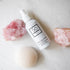 A white bottle of Só Tonic Apple Cider Vinegar facial toning spray, styled on a white marble surface with pink crystal rocks and a cream coloured konjac sponge.