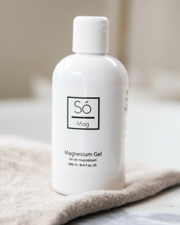 A white bottle of Só Magnesium Gel with on beige fabric with a blurred background.
