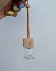 Clear glass bottle with wooden cap branded with Só and beige string held by a hand on a light gray background