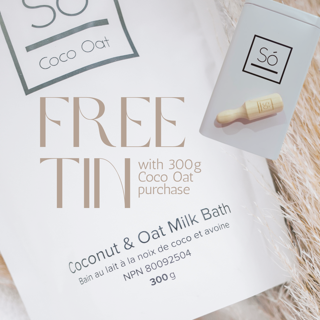 A close-up of a white product package for “FREE TIN” coconut and oat milk bath, with a small white tin shown beside it on a soft beige textured surface. The package text reads “Coconut &amp; Oat Milk Bath,” “300 g,” and the visible brand is “Só
