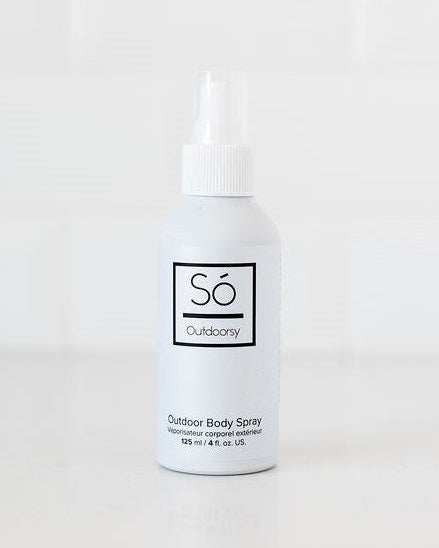 A white bottle of Só Outdoorsy Outdoor Body Spray with a white nozzle cap, standing on a white surface against a white tiled background.
