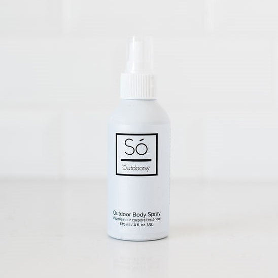 A white bottle of Só Outdoors Outdoor Body Spray with a white nozzle cap, standing on a white surface against a white tiled background.