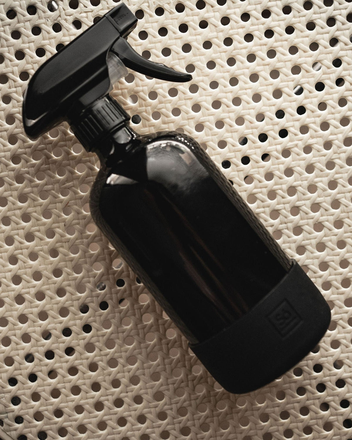 A black glass spray bottle on a rattan surface