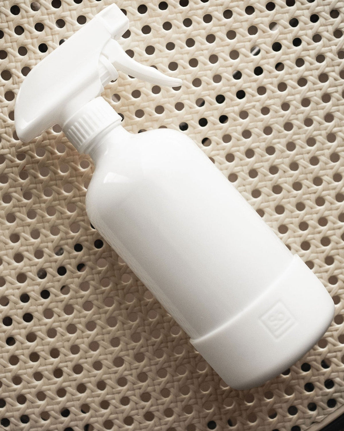 A white glass spray bottle on a rattan surface