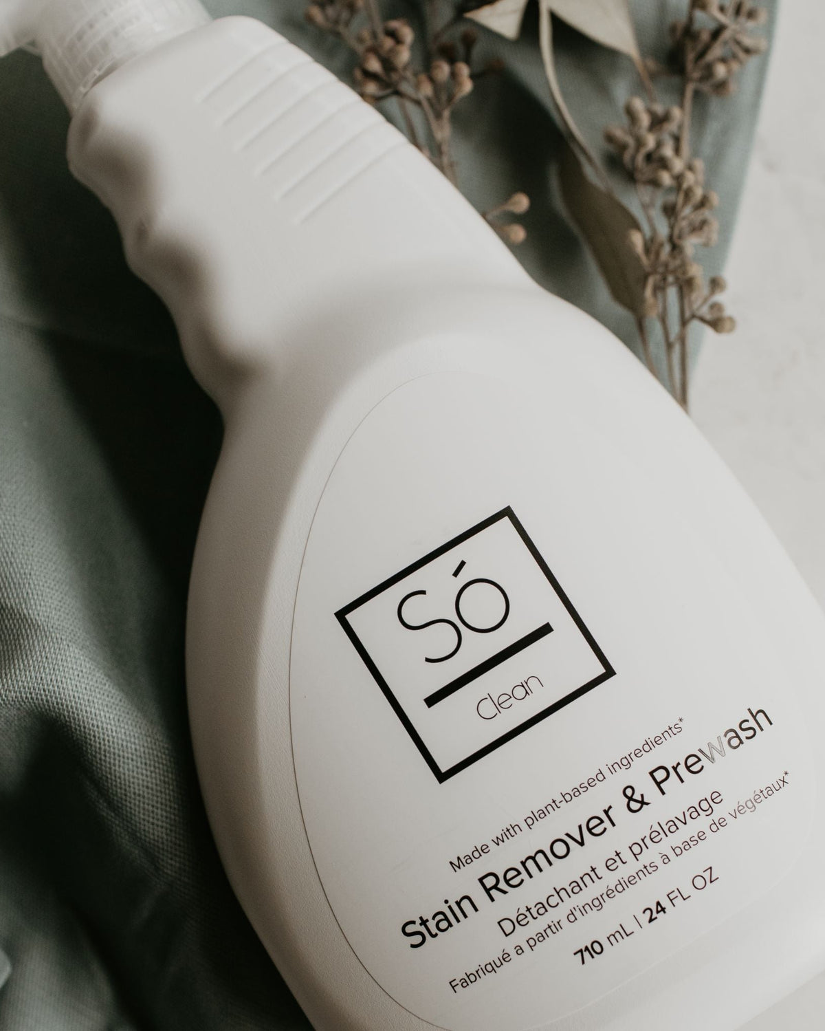 White spray bottle branded with 'Só Clean Stain Remover + Prewash' on a light marble background with green fabric and greenery.
