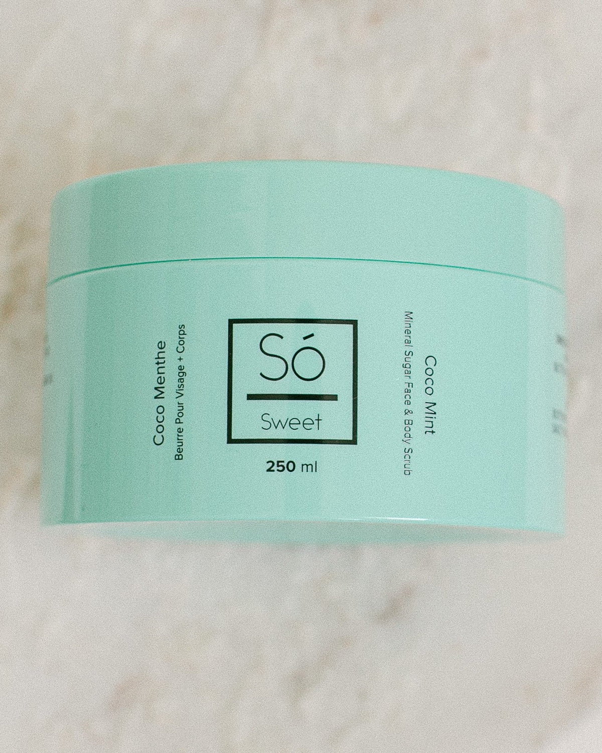 A 250 ml mint green jar of Só Sweet Coco Mint body scrub, resting on a light beige marble surface.