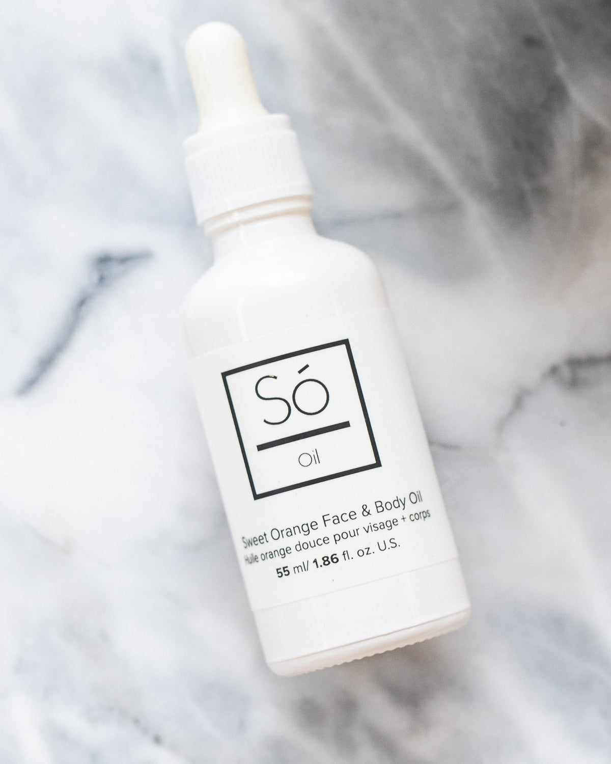 A white bottle with a dropper labeled 'Só Oil Sweet Orange Face & Body Oil' on a grey marble background.