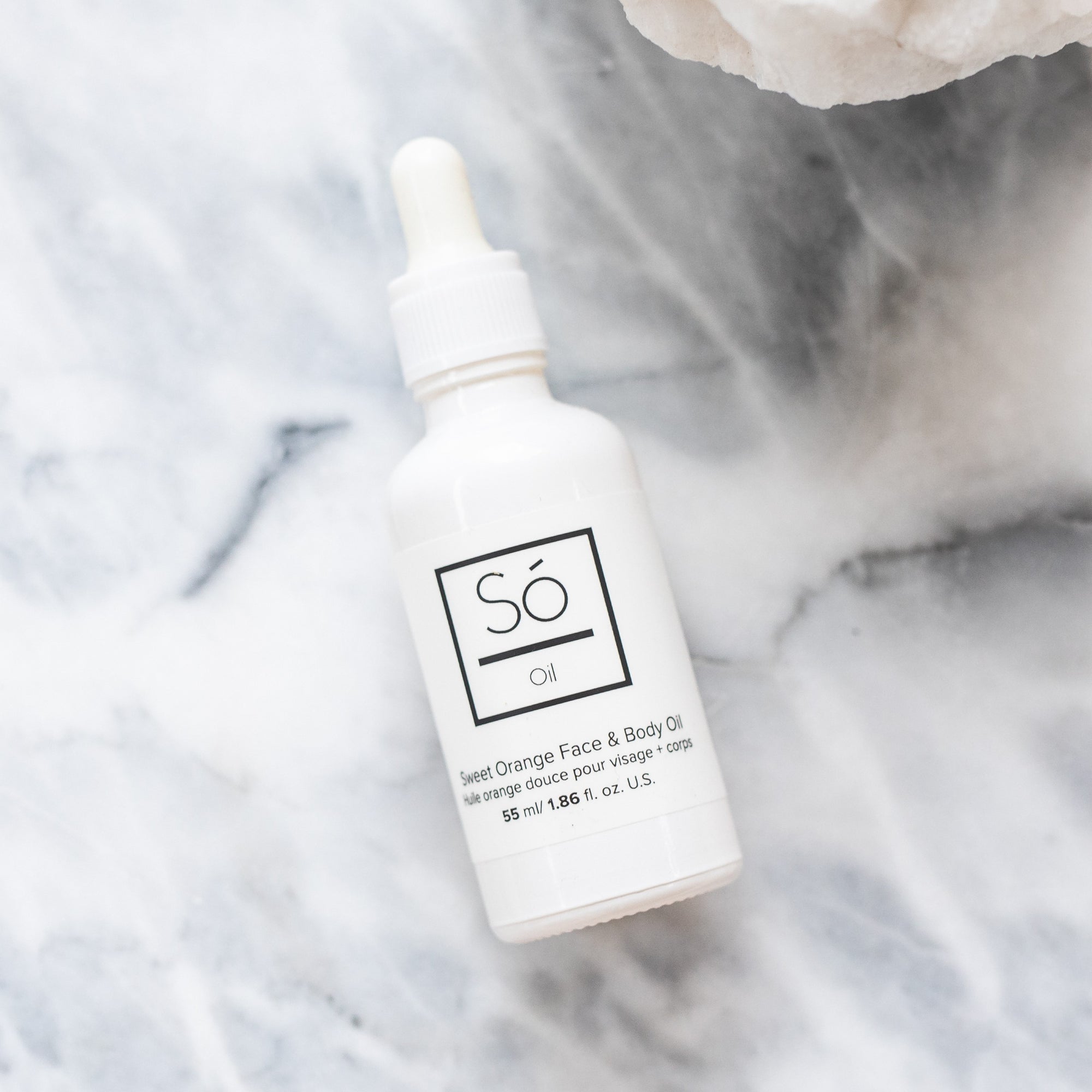 A white bottle with a dropper labeled 'Só Oil Sweet Orange" on a marble backdrop