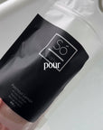 A video depicting a hand holding an open bag of Só Salty Patchouli Lemon over a filling bathtub and pouring pink salt into the tub. Text overlay says "pour. sóak. unwind"
