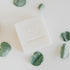 A square white bar of soap with the brand name 'Só' embossed on top, styled on a light background with scattered green eucalyptus leaves.