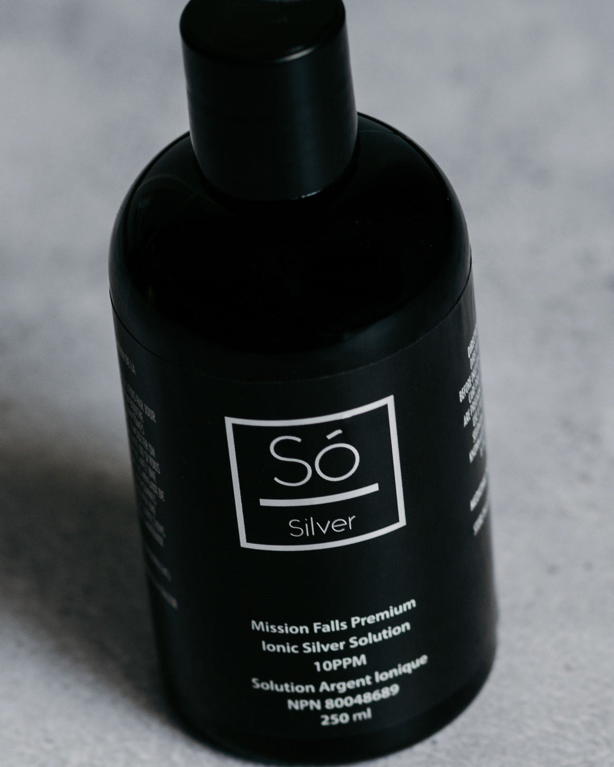A black bottle of Só Silver Mission Falls Premium Ionic Silver Solution, 250 ml, shown on a light gray textured surface.