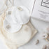 White reusable cotton face pads with small sewn-on 'Só' branded tags, arranged on a cream mesh bag next to a white box on a light marble surface with a few crystals.