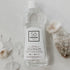 A bottle of Só Clean Citrus Rinse Aid on a marble surface styled with naturlal rocks and flowers.